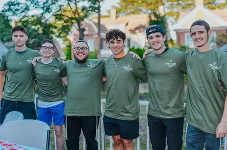 Six young men in green shirts smiling on campus
