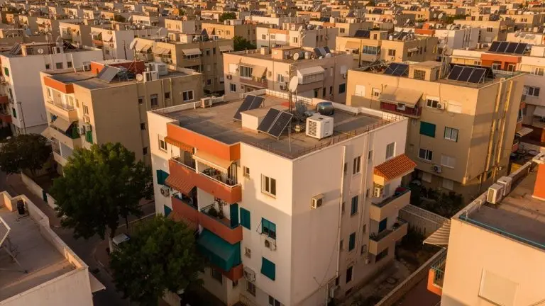 מבט מלמעלה על שכונת מגורים צפופה באור אחר הצהריים, בטורי בניינים עם גגות שטוחים ומרפסות