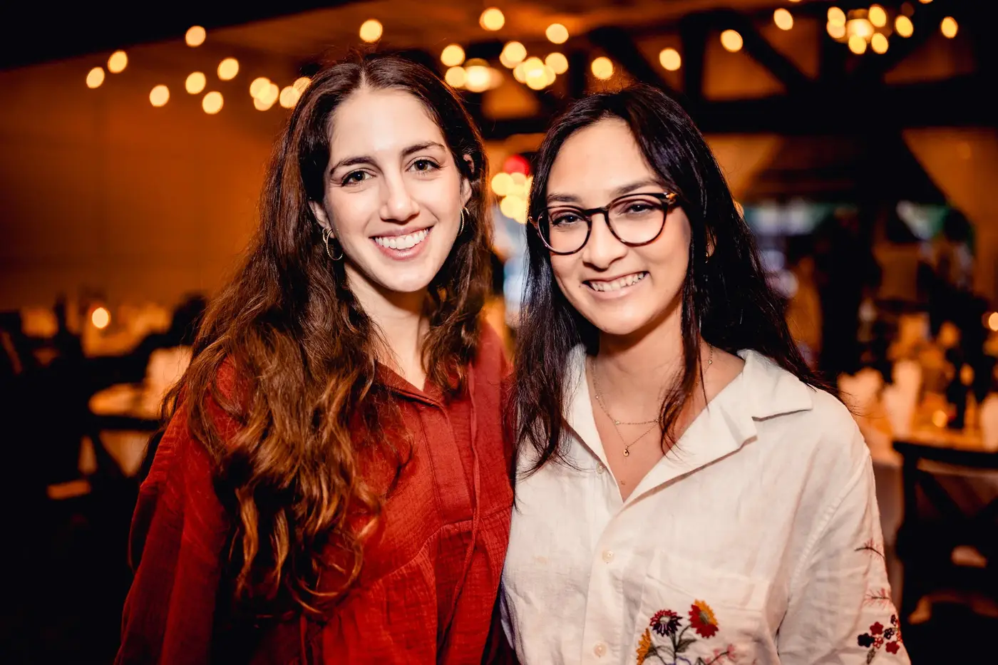 Two women smiling at a social gathering with warm lighting and blurry background.