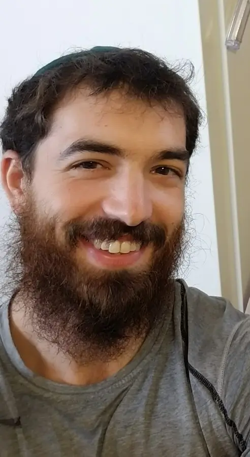 A smiling man with a beard, short dark hair, and wearing a gray athletic shirt taking a selfie indoors.