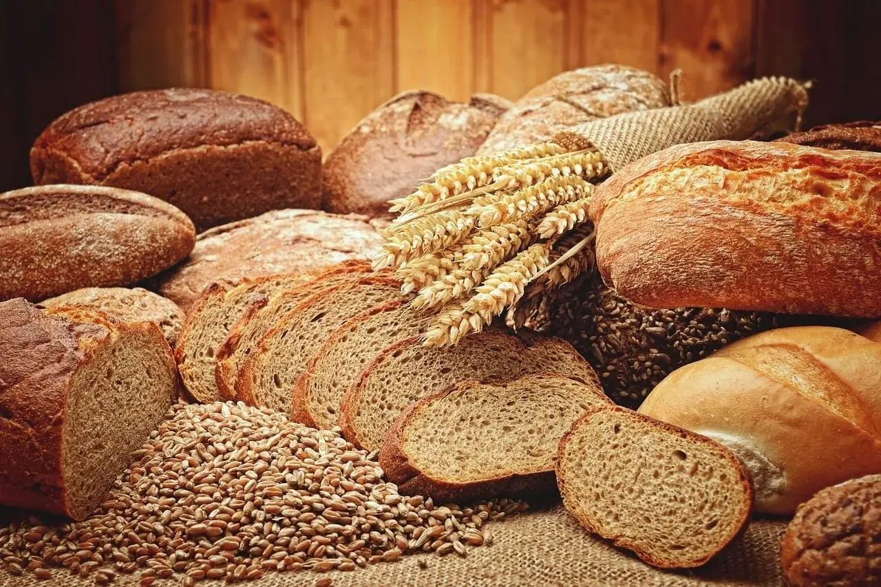 Variety of bread loaves and slices, wheat stalks, and wheat grains on a rustic wooden table.