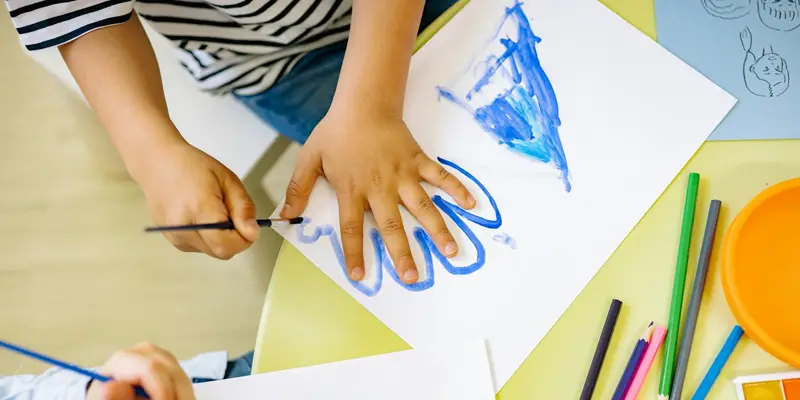 hild painting a blue picture with watercolors at a craft table.