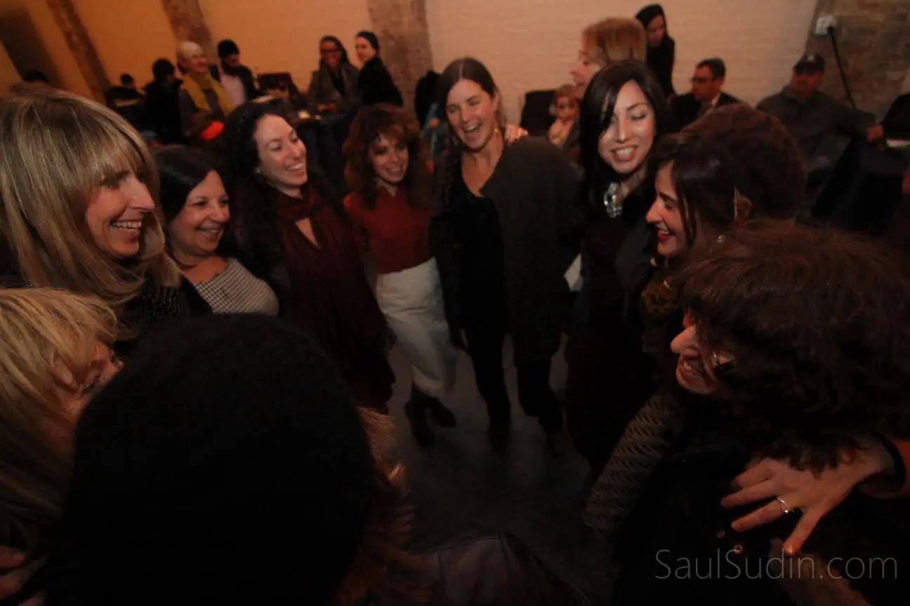 Group of women in a circle, smiling and laughing at a social gathering or party.
